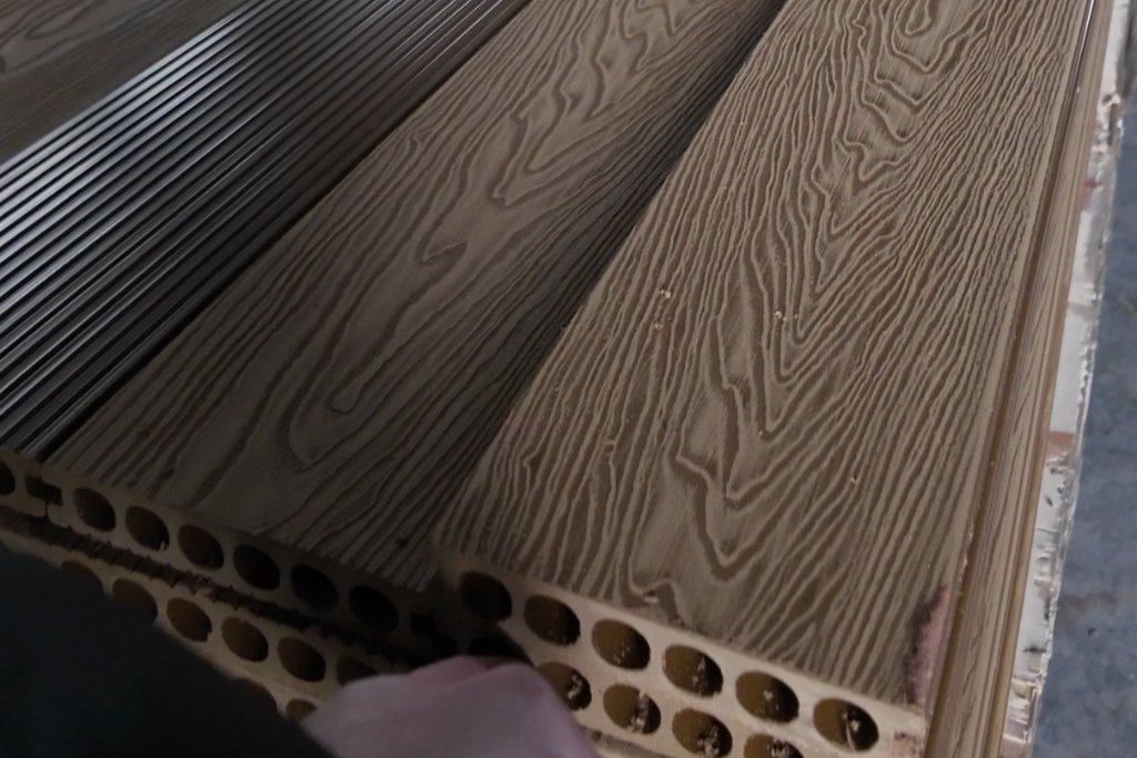 Close-up of hollow-core composite decking boards with wood-grain texture and hand for scale