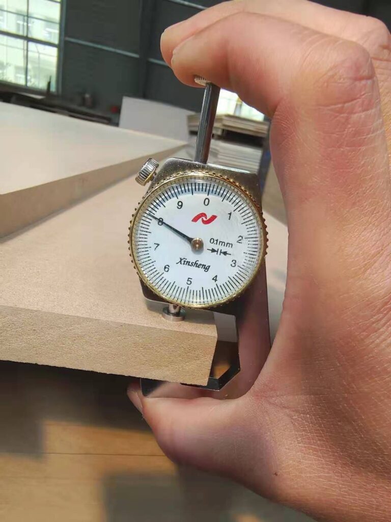 Hand using dial indicator to measure wood panel thickness in workshop