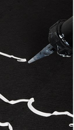 Glue gun dispensing white adhesive onto black surface in precise lines