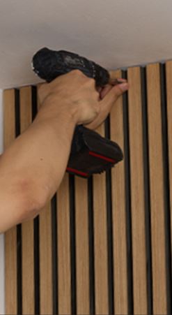 Person installing modern wooden slat ceiling panel with cordless drill