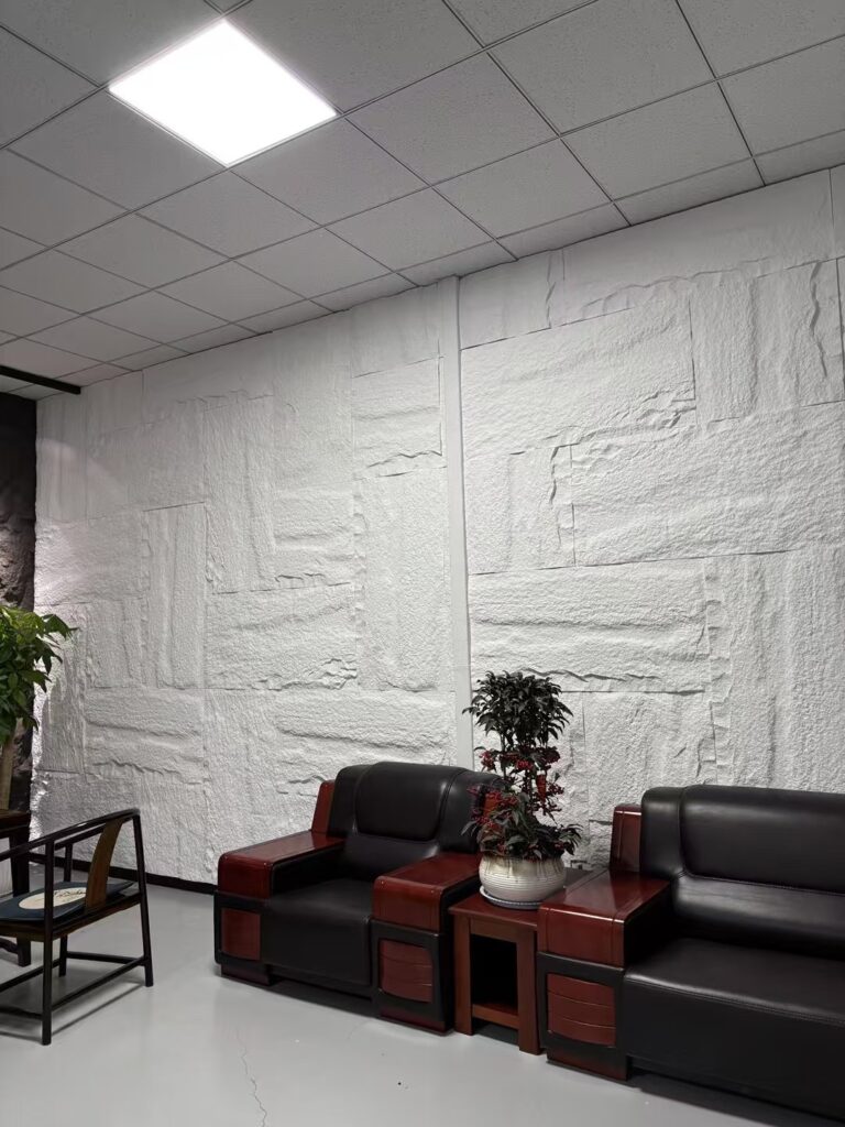 Modern office lounge with textured white wall, leather sofas, wooden tables, and indoor plants