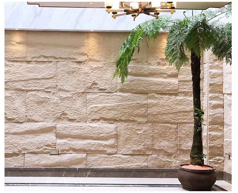 Modern stone wall interior with potted palm, polished floor, and warm chandelier lighting.