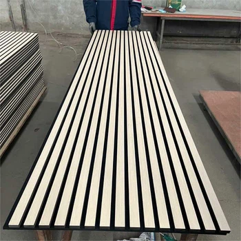 Slatted wooden acoustic panel on workbench in workshop with worker inspecting