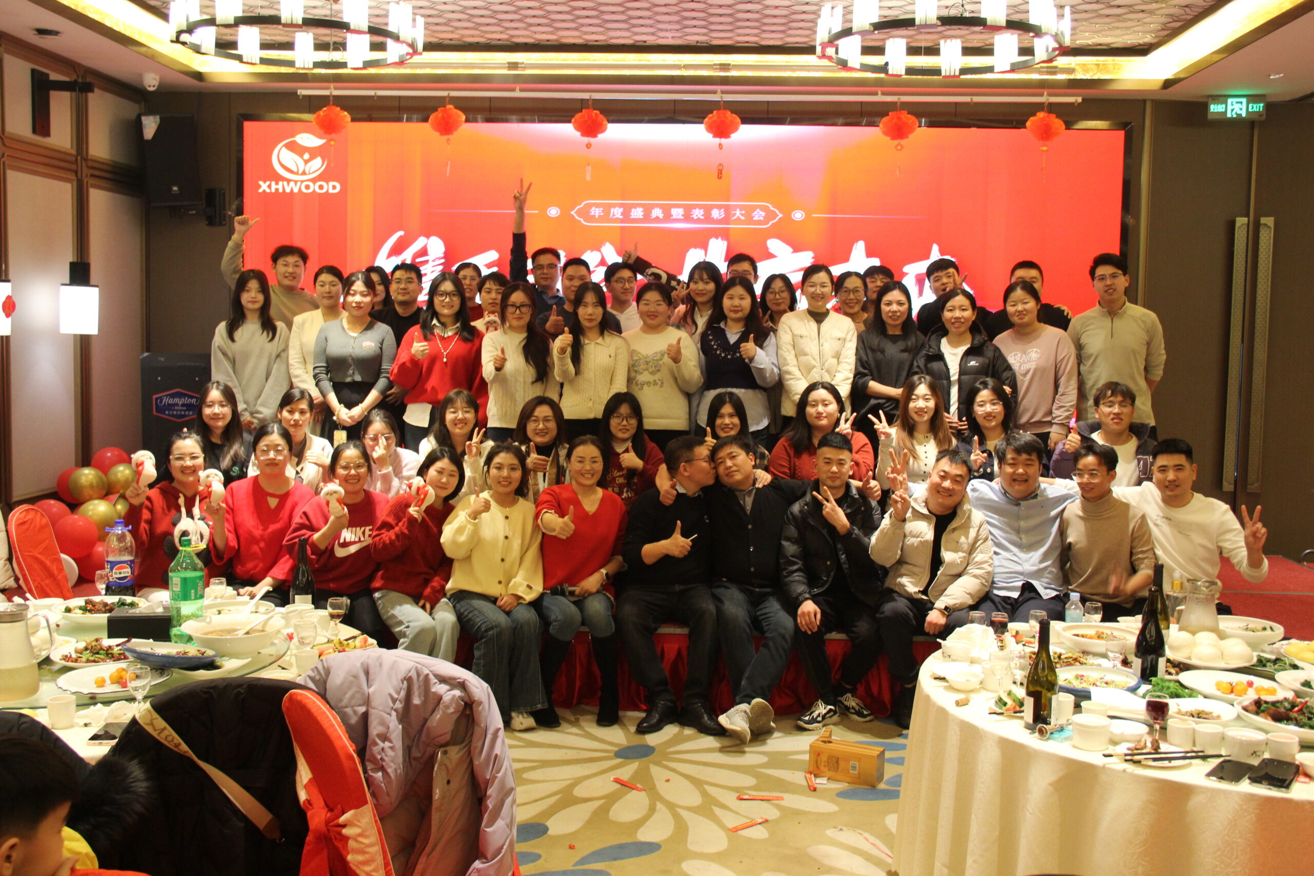 Team group photo at Chinese New Year banquet with red decorations and dining tables.