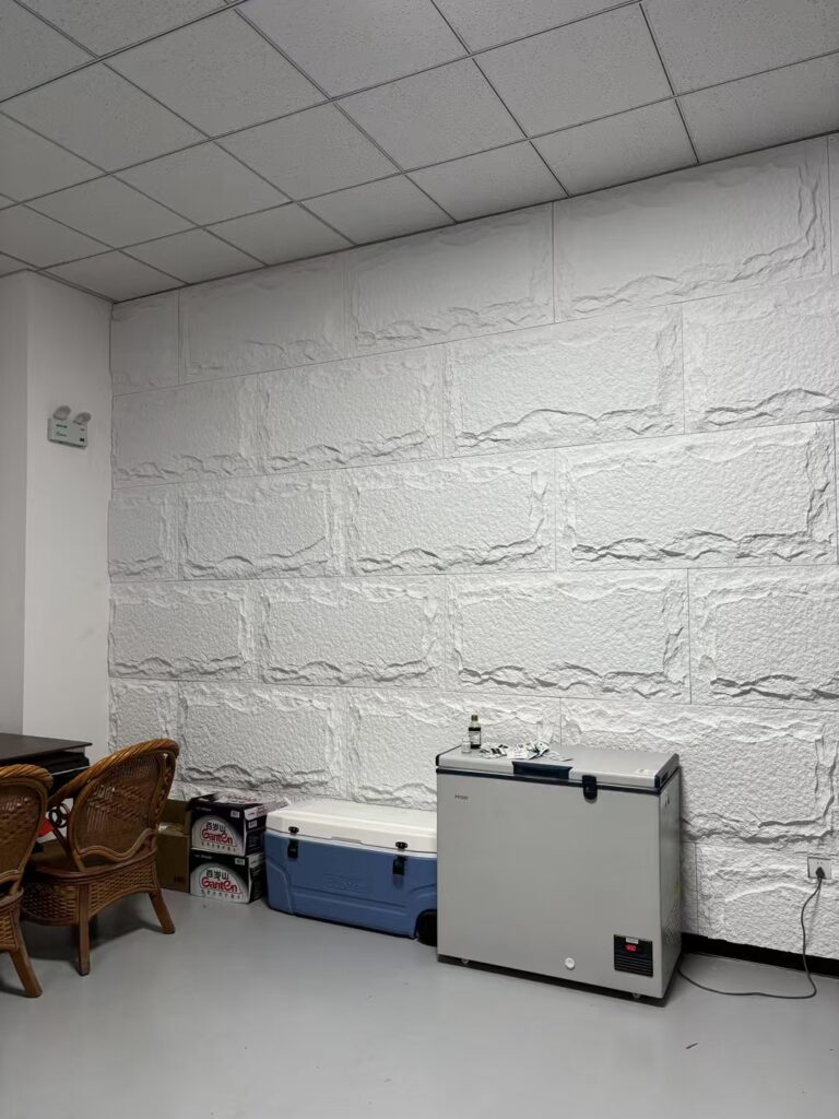 Modern break room with white stone wall panels, wicker chairs, and coolers.