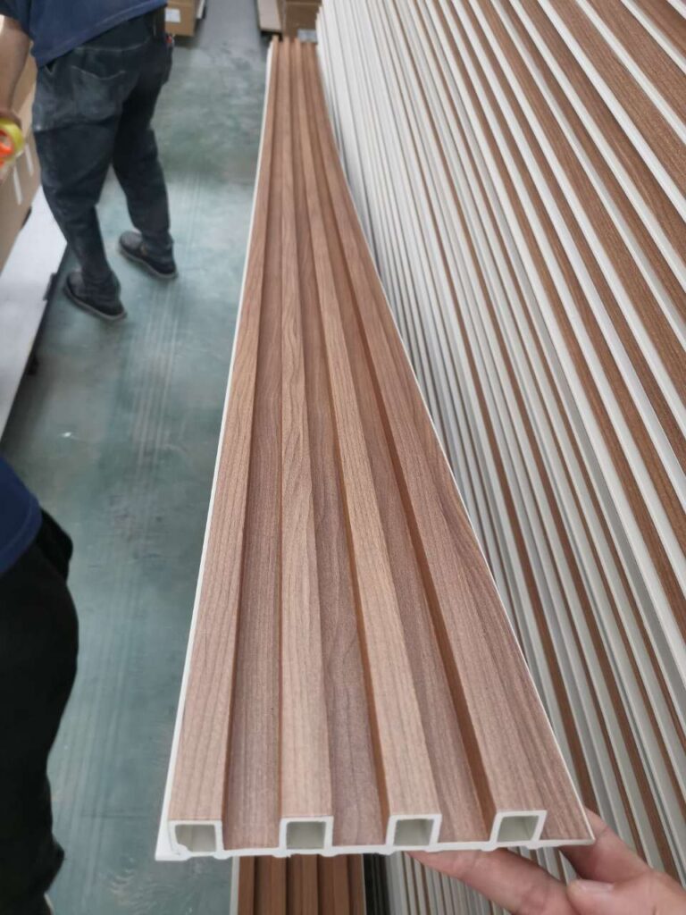 Wood-look PVC slat wall panel held in warehouse with stacked modern panels